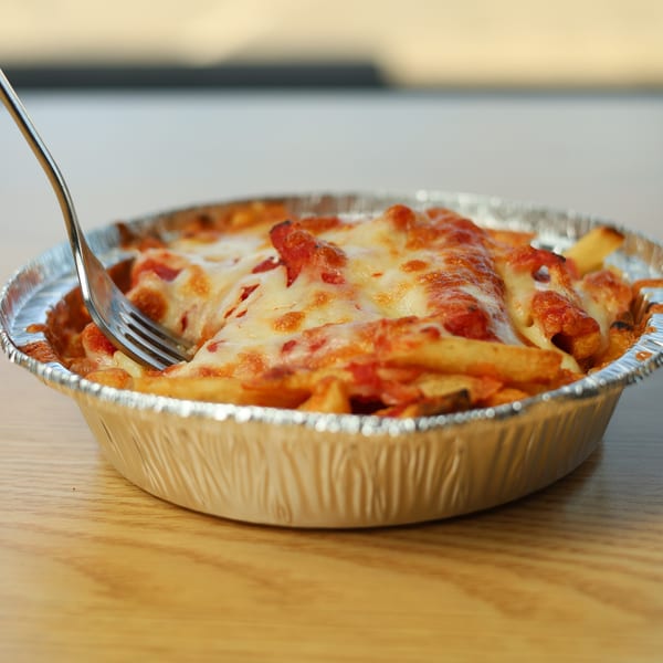 A fork is digging into a foil pan of baked ziti with melted cheese and red sauce.