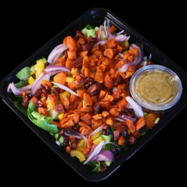 A colorful salad with lettuce, red onions, bell peppers, and dried fruit, with dressing on the side.